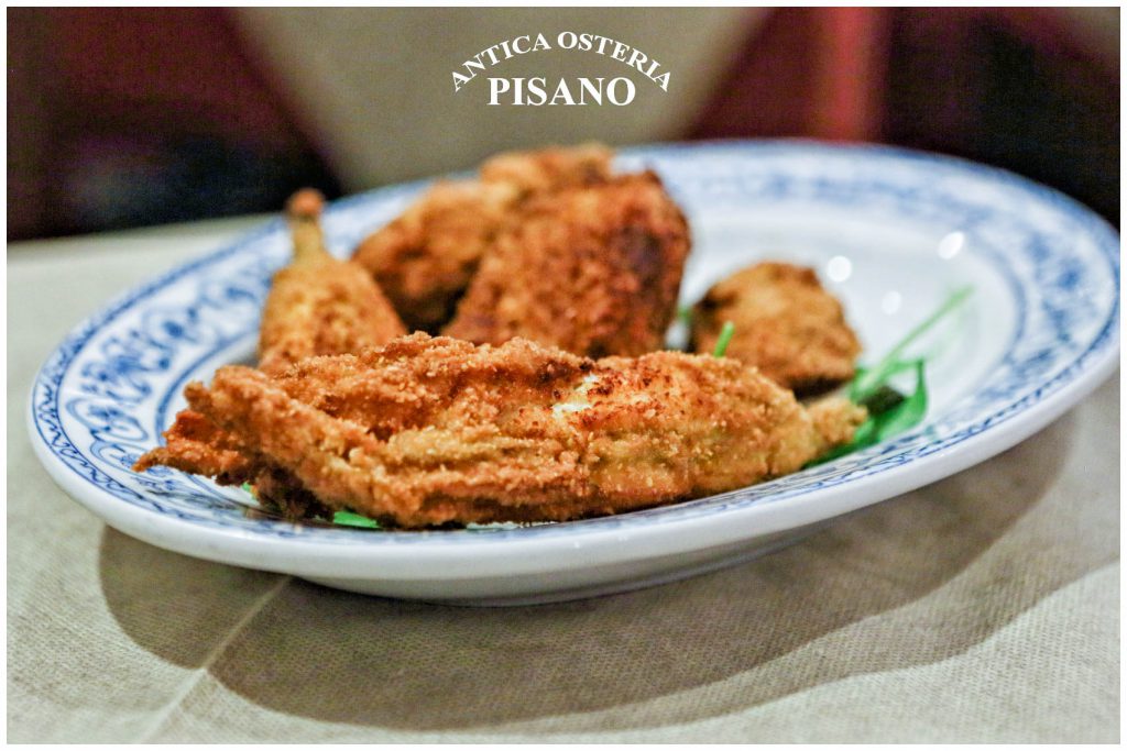 Antica Osteria Pisano: su un piatto bianco con decoro blu ci sono fette impanate dorate e croccanti, con erbe verdi in primo piano.