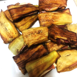 Melanzane fritte ripiene di prosciutto e formaggio, pronte da gustare. Melanzane fritte dorate, tagliate a pezzi e farcite con prosciutto e formaggio, presentate su piatto bianco, piatto della cucina napoletana.