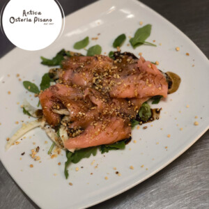 Salmone nocciolato servito su rucola, firmato Antica Osteria Pisano Salmone rosa nappato con croccante di granella di nocciola su letto di rucola, con riduzione di salsa e topping aromatico, riferimento al piatto napoletano di Antica Osteria Pisano