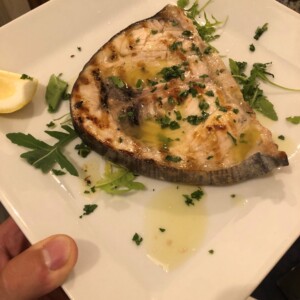 Spada grigliata con olio d'oliva e limone, guarnita con prezzemolo e rucola Spada grigliata con olio d'oliva e prezzemolo, servita su piatto bianco con limone e rucola, ottima presentazione culinaria napoletana