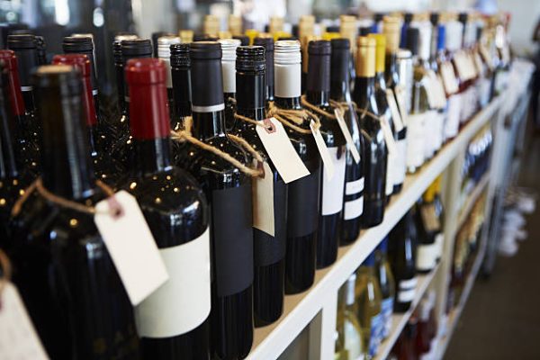 Bottiglie di vino in vetro scuro allineate su scaffale, con etichette legate e tappi di colori differenti, scatto iStockphoto per Antica Osteria Pisano